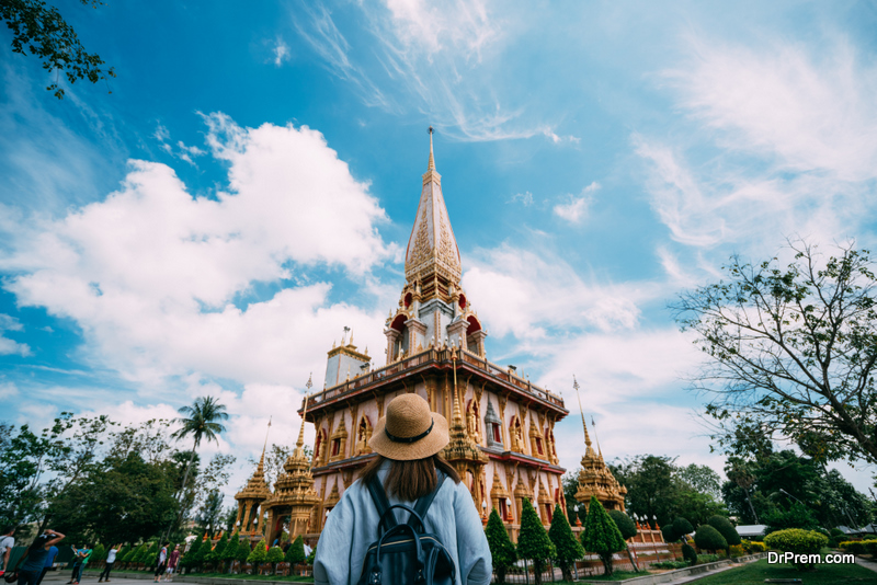 Young woman traveler with backpack traveling into beautiful pagoda in Wat Chalong or Chalong temple at Phuket town, Thailand