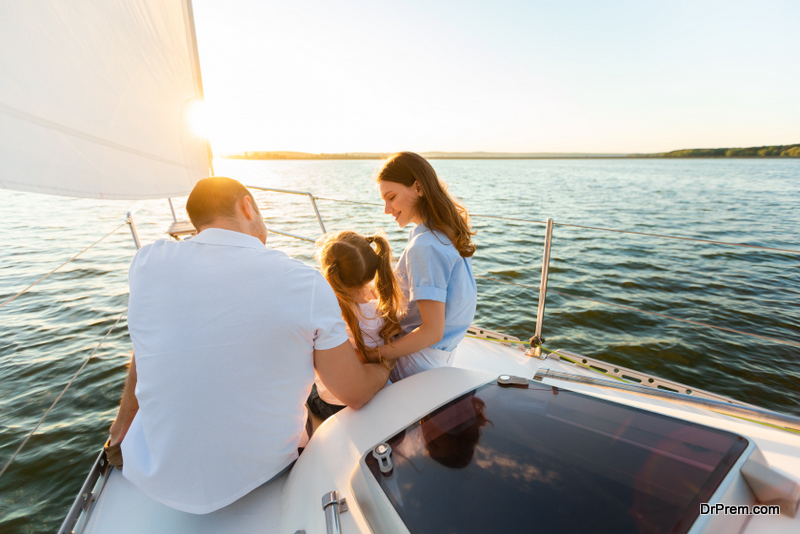 Rear View Of Family Sailing On Yacht Sitting Together On Sailboat Deck